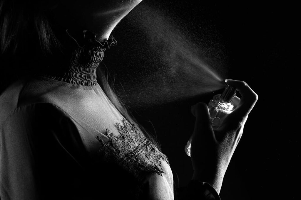 A stylish woman sprays perfume, captured in a dramatic black and white studio shot.