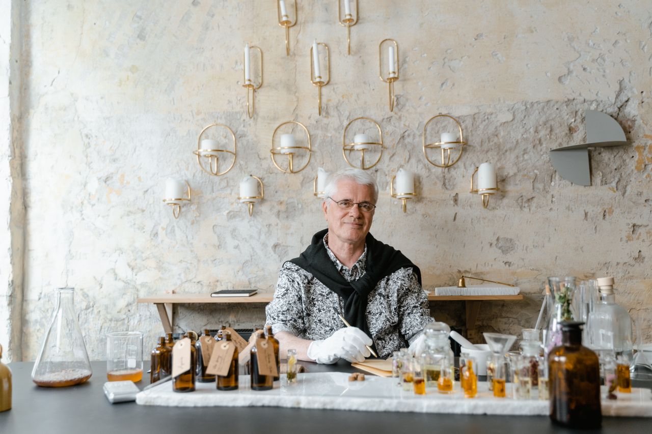 The Art of Drawing Readers In: Your attractive post title goes here Senior male perfumer sitting among fragrance bottles in a rustic setting, creating unique scents.
